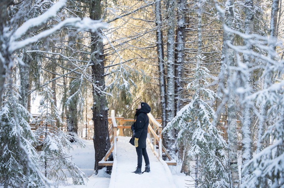 Henkilö kävelemässä talvisella puusillalla metsäisessä ympäristössä Oulussa